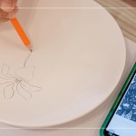 筆尖在素色瓷胚上，輕輕滑過，對(duì)照著手機(jī)上的圖樣，描繪形塑出個(gè)人獨(dú)特的風(fēng)格。