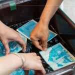 將明信片輕放入水箱中，清洗掉藥水後，隨著雙氧水的洗禮，藍(lán)曬圖像逐漸浮現(xiàn)。